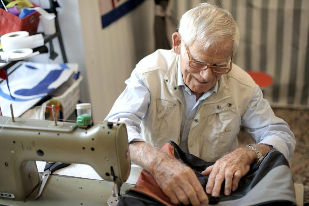 Elderly tailor working on an industrial sewing machine in his workshop, focused on crafting a garment