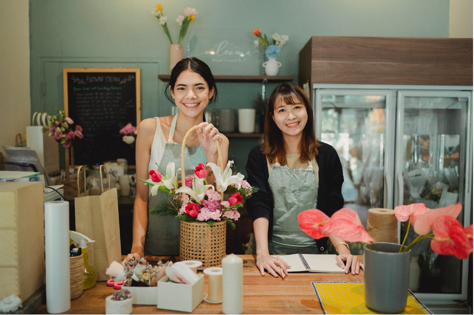 two casual workers in a flower shop, smiling and surrounded by flowers and gifts