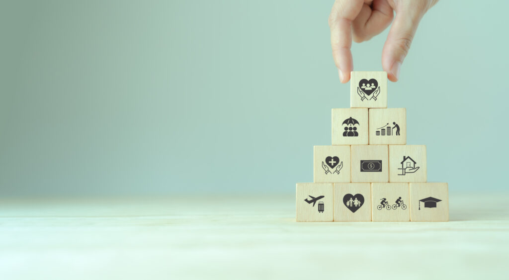A hand completing a pyramid of wooden blocks featuring icons representing various employee benefits and values
